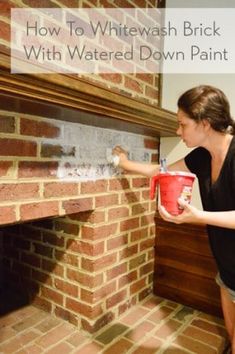 a woman is painting a brick fireplace with a red bucket and white paint on it