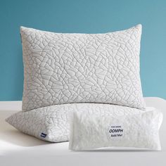 two pillows and a pillow on a bed with blue wall in the backround