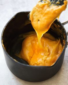 a spoon full of cheese being lifted from a pot