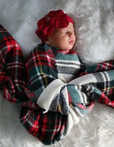 a baby wrapped in plaid is sleeping on a white furnishing with a red headband