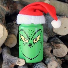 a green grin face jar with a red santa hat on top of it next to logs