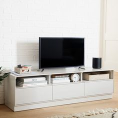 a flat screen tv sitting on top of a white entertainment center next to a potted plant