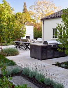 an outdoor kitchen and dining area in a backyard with trees, shrubs, and plants