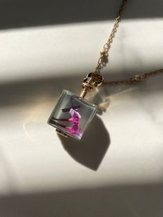 a pink flower in a square glass pendant on a gold plated chain with a white background