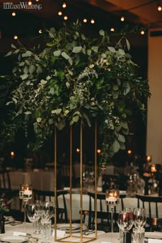 an elegant table setting with candles and greenery in gold vases on the tables