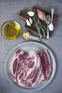 raw meat on a plate with garlic and olive oil next to it, along with other ingredients