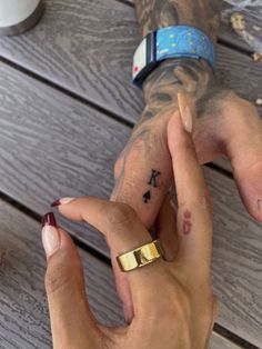 two people holding hands with tattoos on their fingers and one has a gold band around the wrist