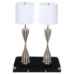 a pair of lamps on a black table with a white lamp in the middle and a gold base