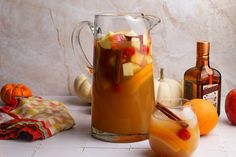 an apple cider with apples, oranges and cinnamon on the table next to it