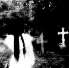 black and white photograph of a woman walking in front of a cemetery with crosses on it