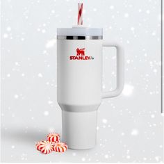 a white travel mug with a candy cane sticking out of it's side next to some peppermints