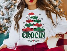 a woman sitting in front of a christmas tree wearing a white sweatshirt and red pants