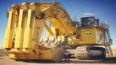 the back end of a large yellow machine in a dirt field with other machinery behind it