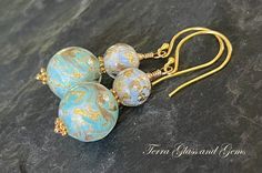 These elegant dangles feature stunning, 12mm, handcrafted Venetian Glass in a marbled, Aqua and Gold, topped with equally stunning, 8mm, Venetian glass beads with gold leaf. All hanging from Gold Vermeil ear wires. All components are gold filled or gold vermeil.  Earrings will arrive in a gift box.  Please ensure that your correct address is listed when you place your order. Terra Glass and Gems is not responsible for lost, stolen, damaged, or misplaced packages. Elegant Handmade Murano Glass Earrings, Elegant Czech Glass Round Earrings, Aqua And Gold, Venetian Glass, Glass Earrings, Earrings Gold, Gold Leaf, Ear Wires, Gold Vermeil