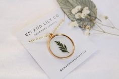 a necklace with a green leaf on it sitting next to a card and some flowers