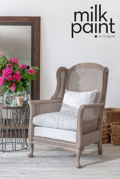 a white chair sitting next to a table with pink flowers on it and a mirror in the background