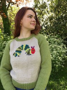 a woman wearing a green and white sweater standing in front of some trees with her hands on her hips