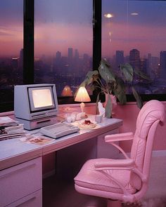 a desk with a computer and a pink chair in front of a window overlooking the city