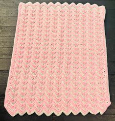 a pink crocheted blanket sitting on top of a wooden floor