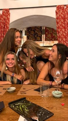 a group of young women sitting around a wooden table with wine glasses in front of them