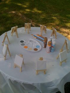 an easel, paintbrushes and other art supplies on a white table cloth