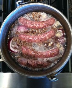 some sausages are cooking in a pan on the stove top with water and spices