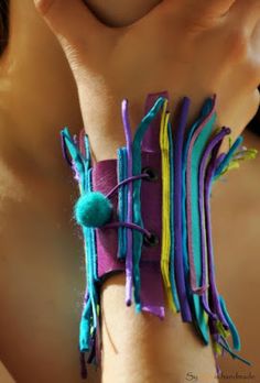 a woman's hand holding a bracelet made out of strips of fabric and felt