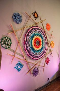 an artistic artwork made from sticks and yarn on the wall in a room with pink lighting