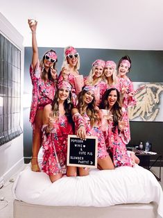 a group of women in matching pink robes posing on a bed with a blackboard