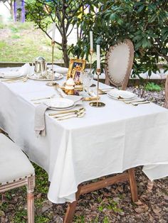 an outdoor table set with white linens and gold place settings for two people to sit at