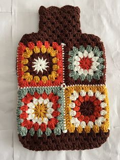 a crocheted pot holder is sitting on a white sheet with a brown, yellow, and red design