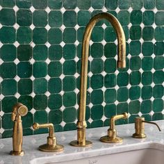 two brass faucets in front of a green mosaic tile backsplash and sink