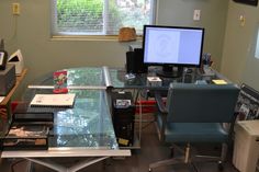 a desk with a computer monitor on top of it next to a chair and other office supplies