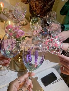 several people holding up wine glasses with flowers in them and confetti on the rims