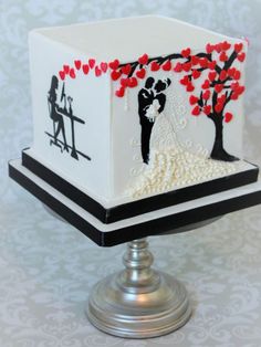 a wedding cake is decorated with red and black hearts on it's sides, while the bride and groom are standing under a tree