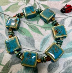 a blue and green bracelet with two red ladybugs on it