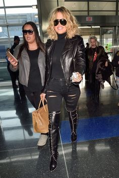 two women walking through an airport with one carrying a purse and the other holding a handbag