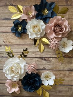 paper flowers are arranged on a wooden surface with gold leaves and pink, blue, white and black ones