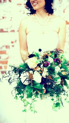 a woman in a wedding dress holding a bouquet with flowers and greenery on it