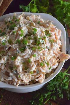 a white bowl filled with chicken salad on top of a wooden table next to parsley