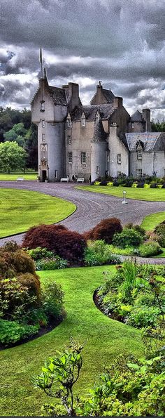 a large house with lots of trees and bushes in front of it on a cloudy day