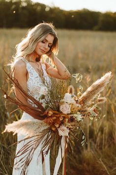 a woman standing in a field holding a bouquet of dried flowers and grass with the sun shining on her face