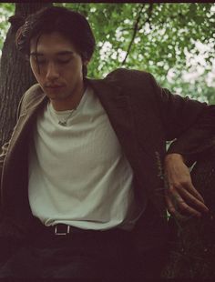 a young man leaning against a tree in the woods