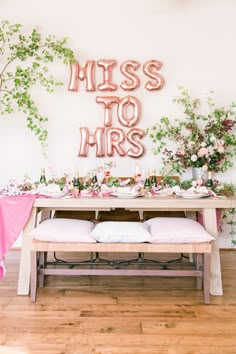 a table set up with pink linens and greenery for a bridal party