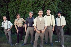 a group of men standing next to each other in front of a green bush with trees