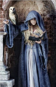 a woman dressed in medieval clothing with an owl on her arm and holding a book