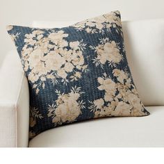 a white couch with a blue and beige floral pillow on it's backrest