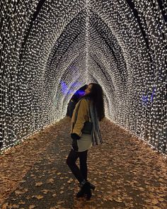 a woman standing in the middle of a tunnel covered with lights