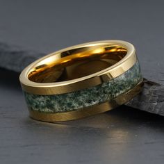 two gold wedding bands with green moss inlays on each band, sitting next to a piece of wood