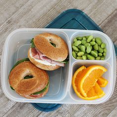 a plastic container filled with two sandwiches and orange wedges next to peas on the side